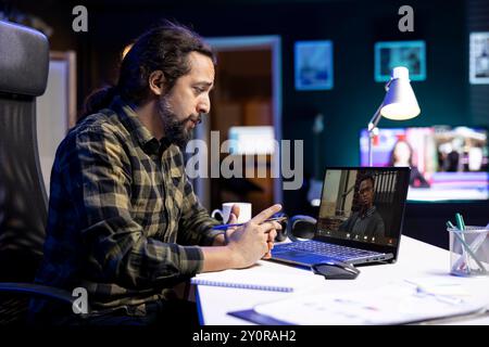 Two multiracial men engaged in a virtual meeting through the laptop. Young bearded man speaking with an individul on a video call, having an online discussion. Stock Photo