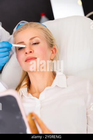 Cosmetologist applying marks on face of young female client Stock Photo