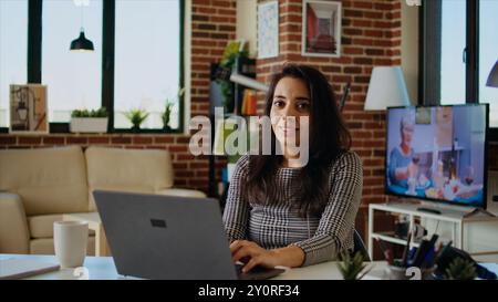 Portrait of smiling remote student typing data on keyboard and taking notes, catching up on homework. Cheerful scholar staying at home doing various tasks at clean wooden desk, camera A Stock Photo