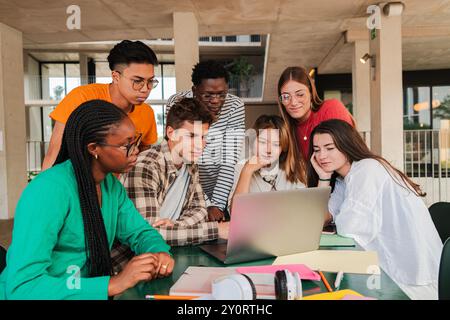 Large team of international young students using a laptop, collaborating on college research task in university campus library. Cooperation of teenagers finding data on notebook for a high school task. High quality photo Stock Photo