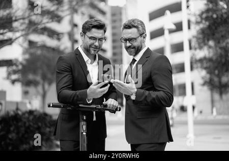 Businessmen using mobile phone outdoor. Confident mature businessman talking on mobile phone while walking outside. Business men looking at messages Stock Photo