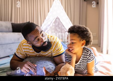 Father and daughter lying on floor, bonding and talking in cozy living room, in teepee Stock Photo