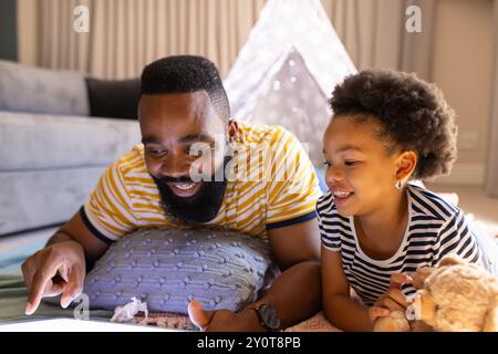 Father and daughter lying on floor, using tablet and smiling at home, in teepee Stock Photo