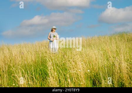Happy mature woman with wildflowers in a tall grass field on a bright summer day. Stock Photo