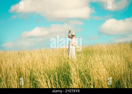 Happy mature woman with wildflowers in a tall grass field on a bright summer day. Stock Photo