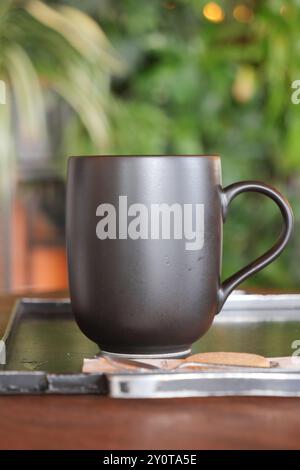 A Stylish Matte Black Coffee Mug Placed on a Beautiful Wooden Table, Perfect for Any Setting Stock Photo