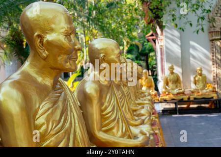 Row of serene golden monk statues in the tranquil setting of a thailand temple courtyard Stock Photo