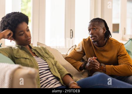 Having serious conversation, African American couple sitting on couch at home, looking concerned Stock Photo