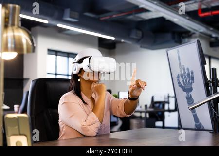 Using VR headset, woman interacting with virtual robotic hand in modern office Stock Photo