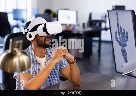 Using VR headset, Indian man interacting with robotic hand design on computer screen Stock Photo