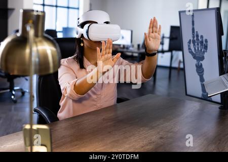 Using VR headset, woman interacting with virtual robotic hand in office Stock Photo