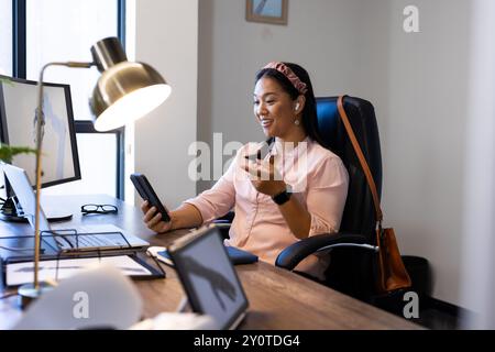 Using tablet and smiling, woman sitting at desk in modern office Stock Photo