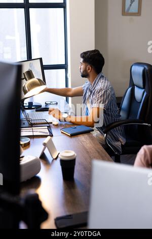 Working in modern office, Indian man using desktop computer and pointing at screen Stock Photo