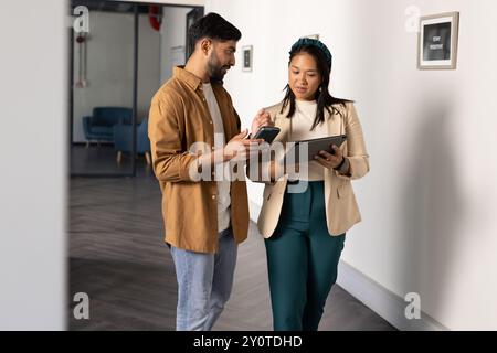 Discussing work, colleagues using smartphone and tablet while walking in office Stock Photo