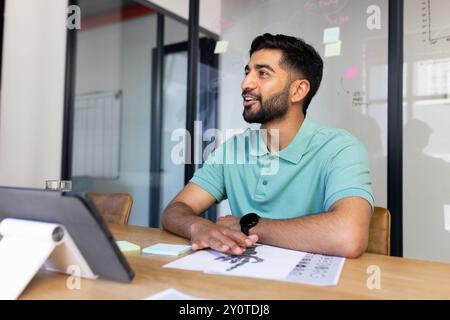 Smiling Indian man in office discussing work, using tablet and documents on desk Stock Photo