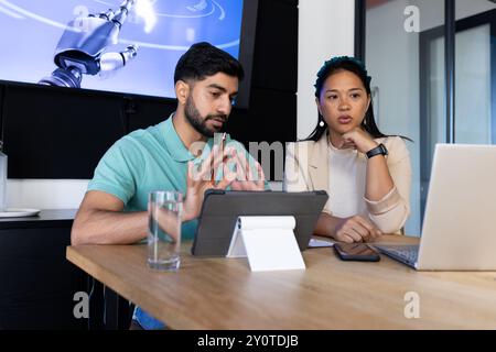 Discussing robotics project, colleagues using tablet and laptop in modern office Stock Photo