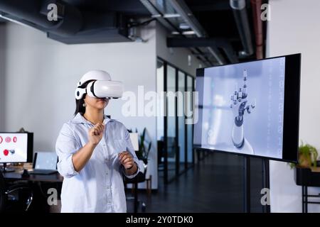 Using VR headset, woman interacting with virtual robotic hand in office Stock Photo