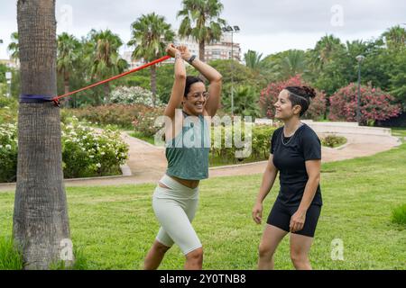 Two women engage in an outdoor personal training session, using resistance bands to perform strength and flexibility exercises in a park. The session Stock Photo