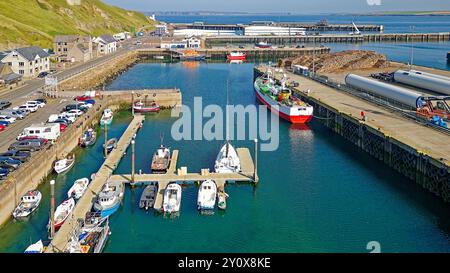 Scrabster Harbour Caithness Scotland the A9 road and small harbour with fishing boats wind turbines and stacked timber Stock Photo