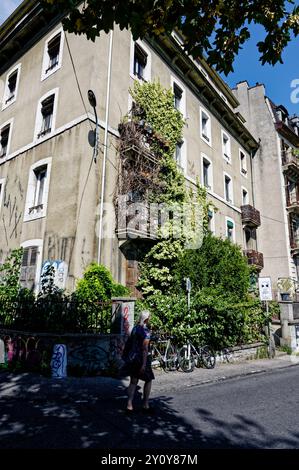 Woman walking past an ivy-covered building on a sunny day in the Grottes Saint-Gervais district Stock Photo