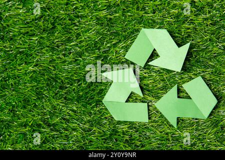 A green recycling symbol on a lush grass background with copy space. Environmental conservation and the importance of recycling concept. Stock Photo