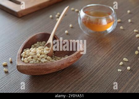 Natural pine nuts in heart shape bowl. Wooden dishes and furniture in kitchen. Fresh clear honey in glass bowl. Healthy products.  Stock Photo