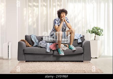 Young man sitting on top of a suitcase on a sofa in a living room and thinking Stock Photo