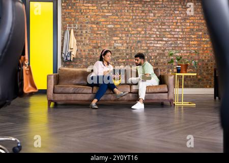 Collaborating on project, colleagues discussing ideas while using laptop on couch Stock Photo
