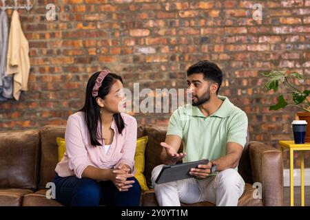 Discussing work, colleagues using digital tablet while sitting on office couch Stock Photo