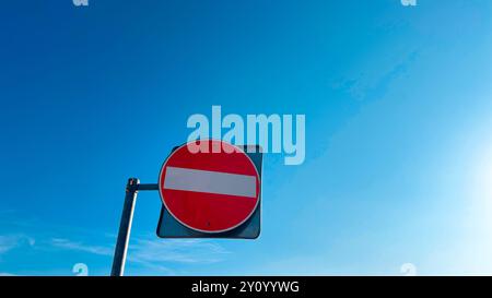 A no-entry road sign against a clear blue sky. The image conveys themes of restriction, prohibition, and guidance, the importance of traffic rules Stock Photo