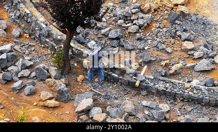 Top view of a construction worker among rocks and rubble, building a stone wall. It highlights labor, resilience, and the meticulous effort Stock Photo