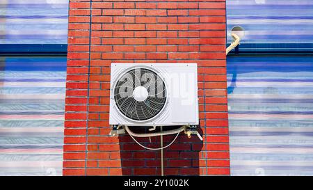 close-up view of an outdoor air conditioner unit mounted on a brick wall. modern technology in energy-efficient cooling and ventilation systems Stock Photo