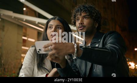 Confused puzzled man woman tourist travelers in night evening city Indian Arabian couple lost in street town travel tour trip guy girl using mobile Stock Photo