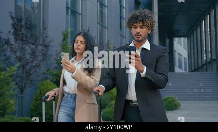 Two business coworkers gadget addict Arabian businesswoman walking city airport terminal using mobile phone Indian businessman browsing typing Stock Photo