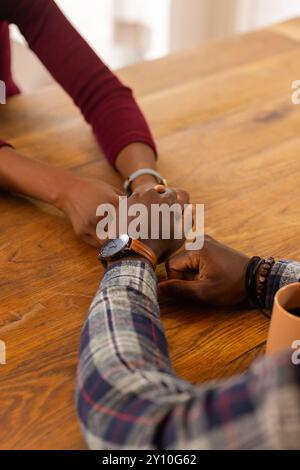 Holding hands, African American couple sitting at wooden table, showing affection and connection Stock Photo
