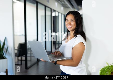 Smiling woman using laptop in modern office, standing near glass partitions, copy space Stock Photo