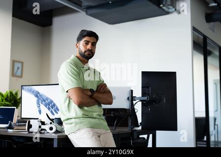Indian man in office leaning on desk with robotic arm image on computer screen, copy space Stock Photo