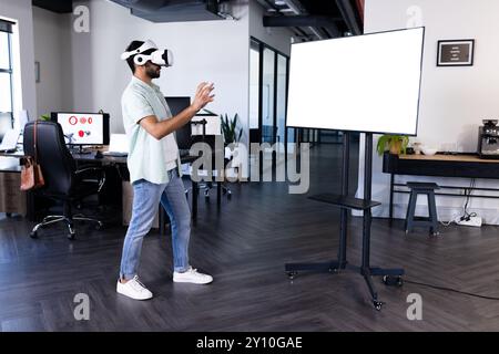 Using vr headset, indian man interacting with virtual display in modern office, copy space Stock Photo