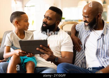 Using tablet, father and son sitting on couch with grandfather smiling Stock Photo