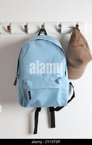 Light blue backpack and cap hanging on white wall Stock Photo