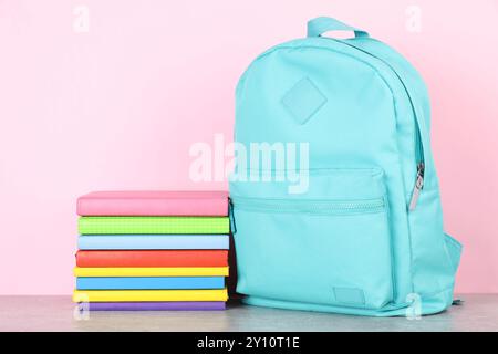 Backpack with different school stationery on light grey table against pink background Stock Photo