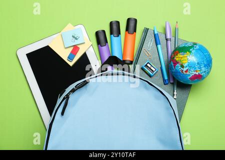 Light blue school backpack with stationery on green background, top view Stock Photo