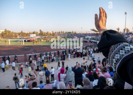 Arabic female watching her son graduation and waving for him while going to get his degree on stage Stock Photo