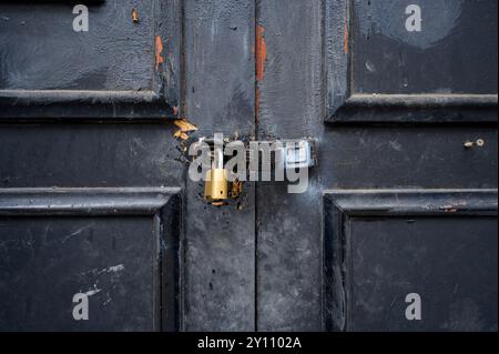 Locked padlock on an old damaged black door, UK Stock Photo