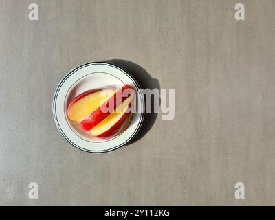 Fresh fruit on a white plate, vitamin-rich diet, healthy fresh apple with red skin cut into slices Stock Photo
