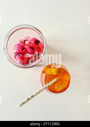 An alcoholic soft drink with straw, ice cubes and orange slice in the glass, refreshment in summer with gummy berries as a snack Stock Photo