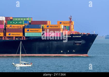 Sailboat sailing past bow of container ship / containership Hudson Express of the Hapag-Lloyd AG shipping company loaded with containers Stock Photo