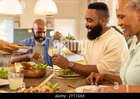 Pouring lemonade, man enjoying meal with multigenerational family at dining table, smiling together Stock Photo