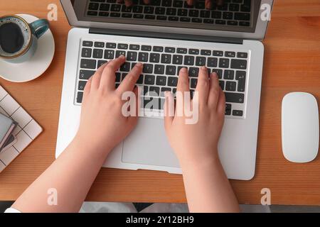 Female programmer using laptop with cup of coffee and mouse on wooden table Stock Photo