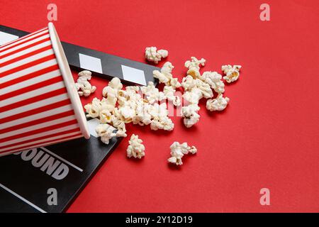 Bucket with tasty popcorn and clapperboard on red background Stock Photo